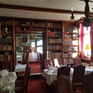 Gastraumit edel eingedeckten Tischen, französischer Bestuhlung, einer großen Bücherregalwand und Messingkronleuchtern