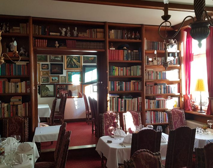 Gastraum mit edel eingedeckten Tischen, französischer Bestuhlung, einer großen Bücherregalwand und Messingkronleuchtern